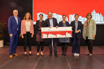 Sieben Personen, die Landesbeauftragten für regionale Landesentwicklung, Ministerinnen Staudte und Osigus und Ministerpräsident Weil, posieren für ein Gruppenfoto. Ministerpräsident und Ministerinnen halten ein Schild mit dem Veranstaltungstitel.