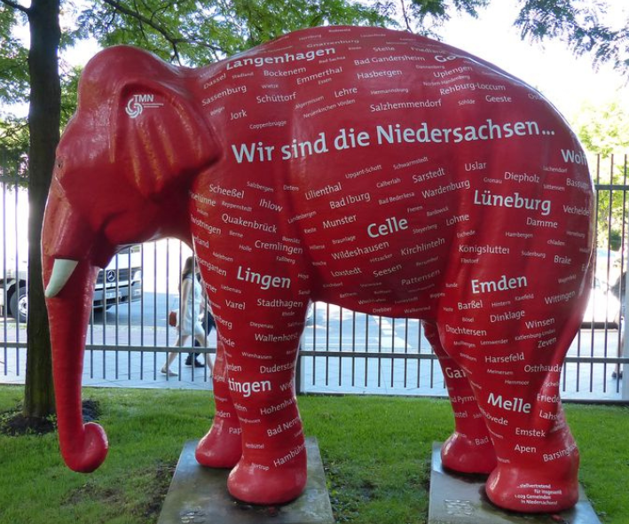 Eine Kunststofffigur eines Elefanten steht auf zwei flachen Sockeln auf einem Stück Rasen. Auf dem Elefanten steht "Wir sind die Niedersachsen.." und die Namen von Städten und Dörfern aus Niedersachsen.