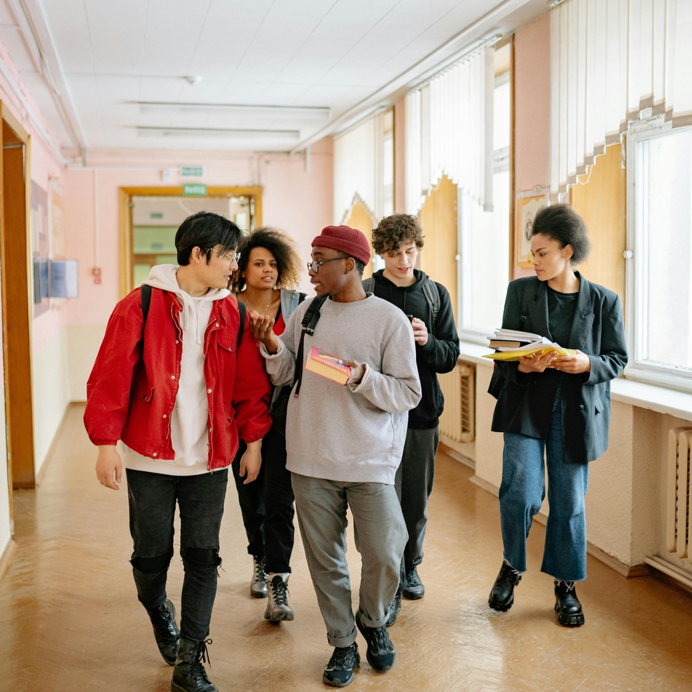 Fünf junge Menschen laufen einen Flur entlang. Sie sind im Gespräch miteinander
